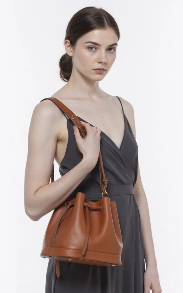 A French female model with a Bucket bag, wearing a dress, against a white background, in a front   facing close   up